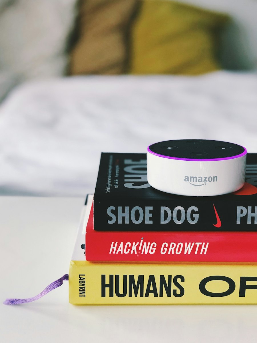 An Amazon Echo Dot resting on a stack of books beside a bed